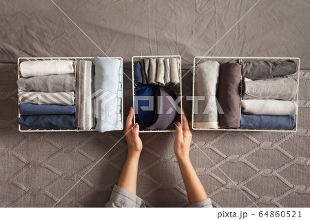 Spring cleaning of closet. Vertical tidying up storage. Neatly folded clothes in the metal white baskets for wardrobe. Grey background. Spring cleaning of closet. Vertical tidying up storage. Neatly folded clothes in the metal white baskets for wardrobe. Grey background. 64860521