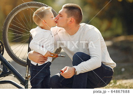 Father with son repare the bike in a park Father with son repare the bike in a park 64867688