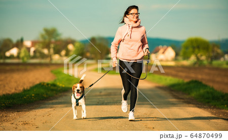 Sport girl is running with a dog (Beagle) on a Sport girl is running with a dog (Beagle) on a 64870499