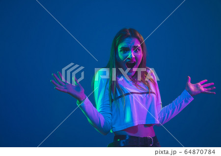 Caucasian woman's portrait isolated on blue studio background in pink-green neon light, stylish and beautiful 64870784