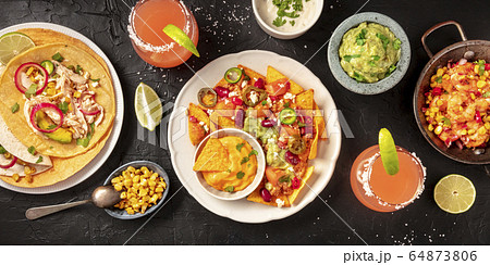 Mexican food, a flat lay panorama on a dark background. Nachos, tortillas, Paloma cocktails, guacamole and other dishes, shot from above 64873806