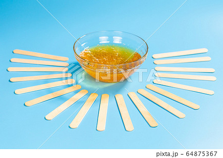 Depilation and beauty concept - sugar paste or honey wax for hair removing spatula with wooden framing sticks on a bright blue background Depilation and beauty concept - sugar paste or honey wax for hair removing spatula with wooden framing sticks on a bright blue background 64875367