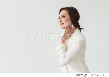 High fashion shoot of young brunette woman with elegant hairstyle in white suit indoors. Business people and trendy style concept. Copy space. High fashion shoot of young brunette woman with elegant hairstyle in white suit indoors. Business people and trendy style concept. Copy space. 64875948