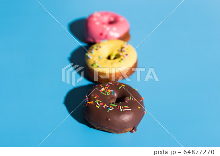 Colourful round donuts at bright blue background. Sweet donuts. Trendy sunlight Summer pattern Minimal summer concept. 64877270