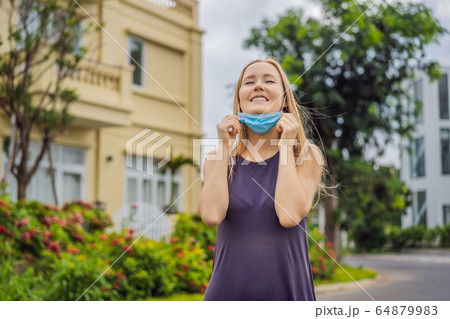 Quarantine is over concept. Woman taking off mask against the background of small town houses. We 64879983
