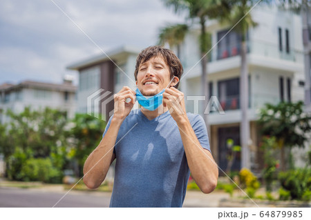Quarantine is over concept. Man taking off mask against the background of small town houses. We are 64879985