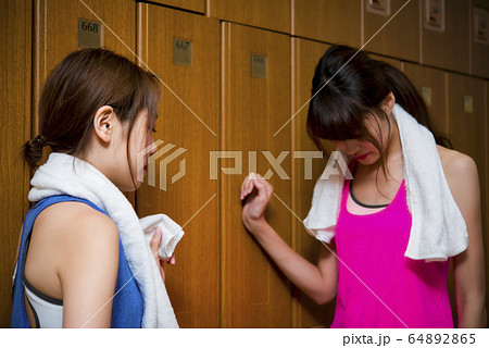 スポーツジムのロッカーで話をする若い女性 64892865