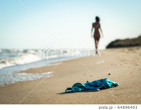 swimsuit in the sand on the beach near the sea surf on the background of a naked female figure and blue sky 64896403