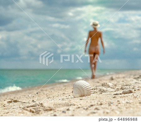 young nude girl with a hat walks on an empty beach near the sea surf against the blue sky with clouds in summer young nude girl with a hat walks on an empty beach near the sea surf against the blue sky with clouds in summer 64896988