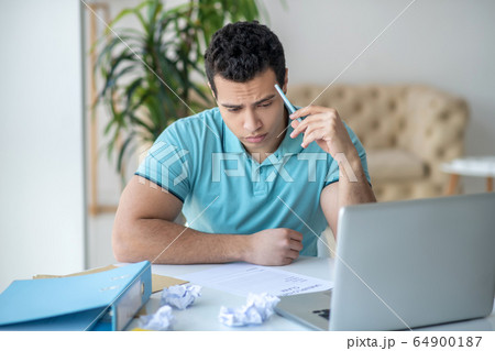 Upset dark-haired male sitting at his desk, filling in unemployment claim 64900187