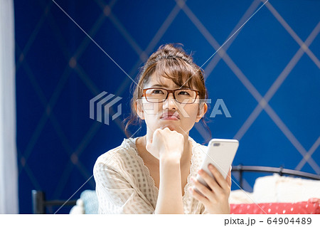 女性　寝室　ベッド　スマホ　不機嫌 64904489