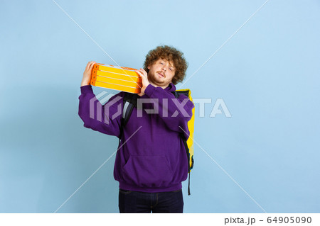 Contacless delivery service during quarantine. Man delivers food and shopping bags during insulation. Emotions of deliveryman isolated on blue background. 64905090