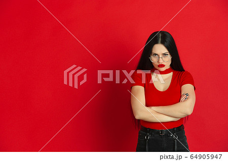 Caucasian young woman's monochrome portrait on red studio background, emotional and expressive 64905947