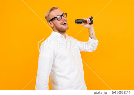 blond guy in a white shirt sings into a retro microphone on a yellow background with copy space 64909874