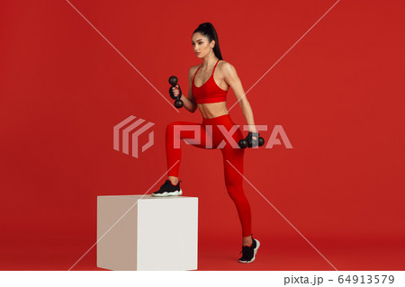 Beautiful young female athlete practicing on red studio background, monochrome portrait Beautiful young female athlete practicing on red studio background, monochrome portrait 64913579