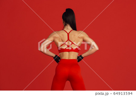Beautiful young female athlete practicing on red studio background, monochrome portrait Beautiful young female athlete practicing on red studio background, monochrome portrait 64913594