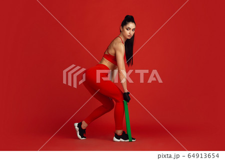 Beautiful young female athlete practicing on red studio background, monochrome portrait 64913654