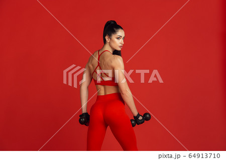Beautiful young female athlete practicing on red studio background, monochrome portrait Beautiful young female athlete practicing on red studio background, monochrome portrait 64913710