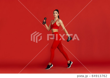 Beautiful young female athlete practicing on red studio background, monochrome portrait 64913762