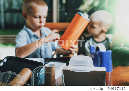 Different recycled materials on desk and blurred kids making crafts from it on the background. 64917112