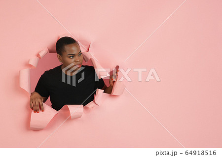Cheerful young woman poses in torn coral paper hole background, emotional and expressive 64918516