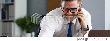 Joyful man in office speaks on phone near laptop 64920321