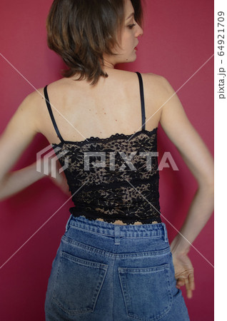 Back view of young woman with short hair dressed in black lace bustier and blue jeans is posing in the studio on bright pink background Back view of young woman with short hair dressed in black lace bustier and blue jeans is posing in the studio on bright pink background 64921709