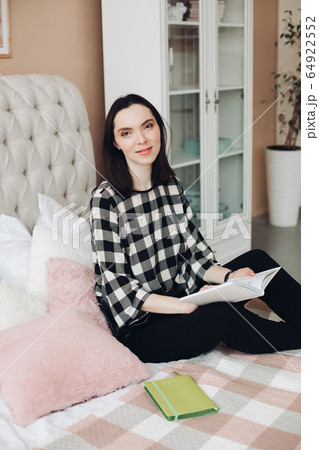 Handsome young woman sits on her bed and reads an Handsome young woman sits on her bed and reads an 64922552