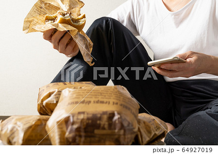 床に寝そべってハンバーガーを食う女 ぐうたら女 干物女 過食症イメージの写真素材