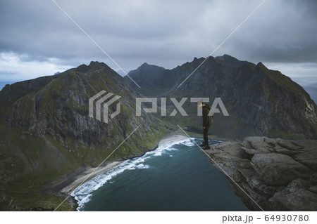 Man standing on cliff at Ryten mountain in Lofoten Islands, Norway 64930780