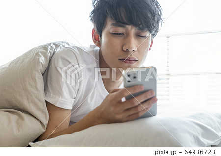 布団の中でスマホを見る若い男性の写真素材