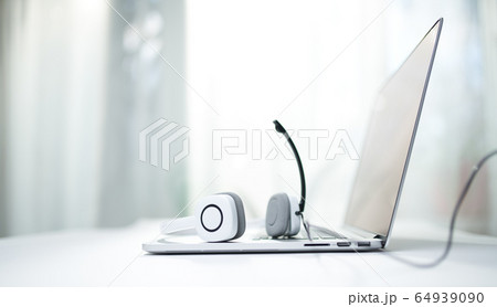 Close-up of laptop, white headphones with microphone on bokeh background. 64939090