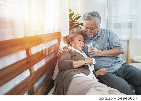 Asian Senior Woman taking medicines and drinking water while sitting on couch.  64940057