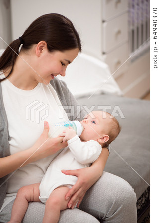 Happy smiling mother and baby stting on bed at home and the baby eats milk. 64940370