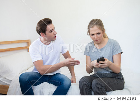 caucasian couple argue with phone on bed at home 64942191