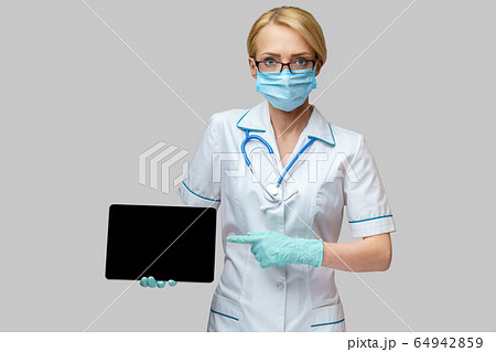 medical doctor nurse woman wearing protective mask and gloves - holding tablet pc medical doctor nurse woman wearing protective mask and gloves - holding tablet pc 64942859