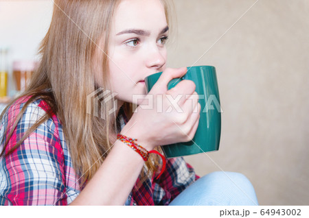 Attractive blonde girl is drinking tea from a large green mug in the kitchen. The concept of spending time during self-isolation of a virus pandemic Attractive blonde girl is drinking tea from a large green mug in the kitchen. The concept of spending time during self-isolation of a virus pandemic 64943002