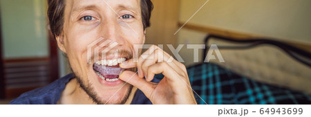Man placing a bite plate in his mouth to protect his teeth at night from grinding caused by bruxism Man placing a bite plate in his mouth to protect his teeth at night from grinding caused by bruxism 64943699