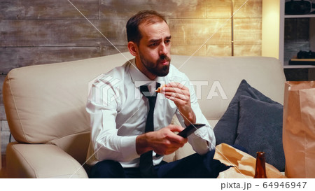 Businessman with tie eating a burger while watching tv Businessman with tie eating a burger while watching tv 64946947