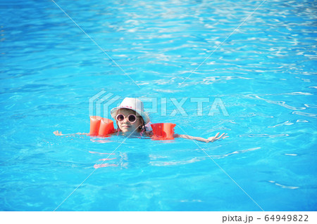 A charming child of European appearance, a girl 7-8 years old, swimming in the pool. Summer, a clear and sunny day. A girl with her family on vacation at sea. The girl has inflatable arm ruffles 64949822