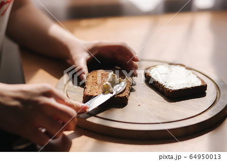 Close up of female butter the rye toasted bread by vegan butter. Woman butter toast at home on wooden board 64950013