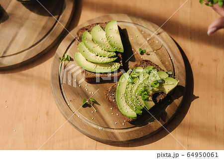 Woman put mustard seedlings on avocado sandwich with dark rye bread made with fresh sliced avocados from above with sesame seeds 64950061
