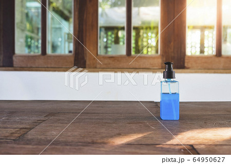 Blue Ethyl alcohol gel or hand sanitizer for coronavirus (COVID-19) protection. in the plastic bottle on the wooden desk in front of the windows with flare light Blue Ethyl alcohol gel or hand sanitizer for coronavirus (COVID-19) protection. in the plastic bottle on the wooden desk in front of the windows with flare light 64950627