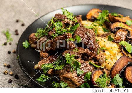 Stewed beef with mushrooms and a side dish of lentils on a black plate. Close-up Stewed beef with mushrooms and a side dish of lentils on a black plate. Close-up 64954161