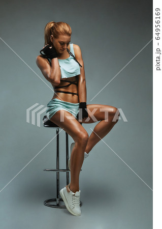 Portrait of a beautiful red-haired, woman in the studio, sitting on the bar counter body shirt. Fashion shooting, gray background. Portrait of a beautiful red-haired, woman in the studio, sitting on the bar counter body shirt. Fashion shooting, gray background. 64956169