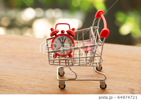Fast delivery, time value of money concept : Red analog clock in a red - silver shopping cart or a supermarket shopping basket on wooden table. depicts the importance of time in our daily life. 64974721
