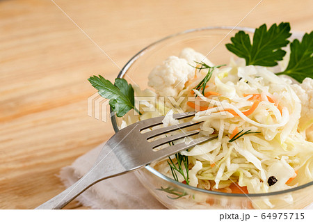 Close-up sauerkraut salad with fresh herbs and fork in glass bowl is standing on light wooden table. Healthy fermented food. 64975715