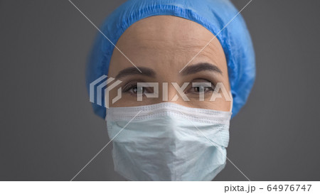 Female Medic In Protective Mask And Blue Cap, Close Up Face Isolated On Grey Back Female Medic In Protective Mask And Blue Cap, Close Up Face Isolated On Grey Back 64976747