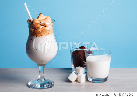 Dalgona korean Iced Coffee, a trendy fluffy creamy whipped coffee with ice on a white wooden table. trendy coffee drink on a blue background 64977250
