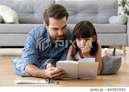 Cute little daughter listening to dad reading book at home Cute little daughter listening to dad reading book at home 64982093